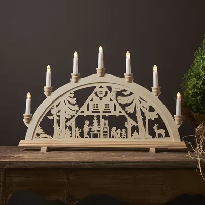 A wooden Christmas arch with LED candles sits on a wooden table.