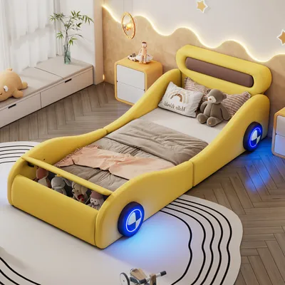 A child's bedroom with a yellow car-shaped bed as the main focus. The bed is made up with bedding and stuffed animals. There are nightstands and a window bench in the background.