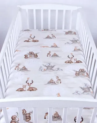 A crib sheet with a woodland animal pattern is laid out flat inside a white crib.