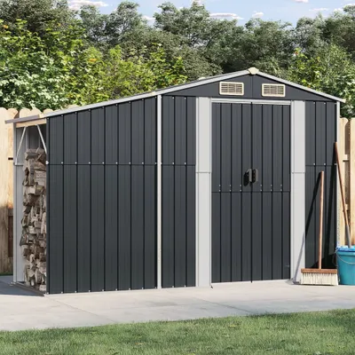 A dark gray metal shed with double doors and a side storage area for firewood, set in a backyard with a concrete path and grass.