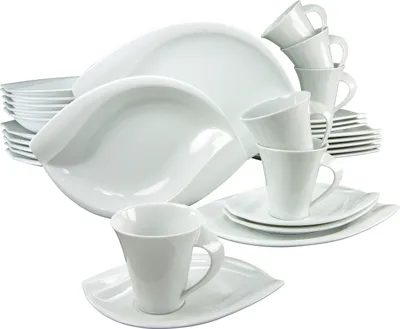 A collection of white porcelain dinnerware, including plates, bowls, and cups, arranged in a studio setting against a white background.
