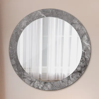 A round mirror with a marble-effect frame is mounted on a light pink wall.