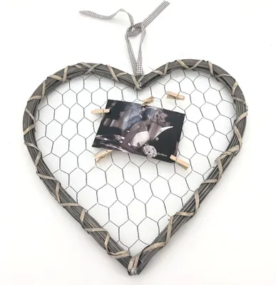 A heart-shaped photo frame made of woven wood and chicken wire, with a wedding photo clipped to it.