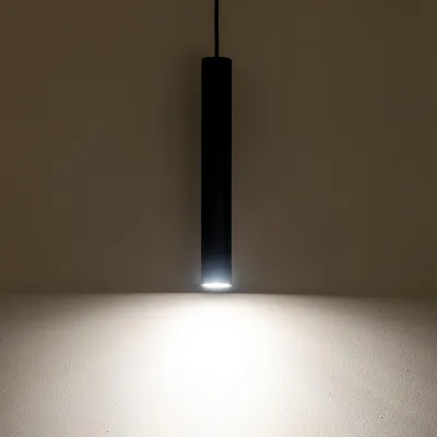 A black cylindrical pendant light is shown hanging against a light-colored wall, illuminating the wall below.