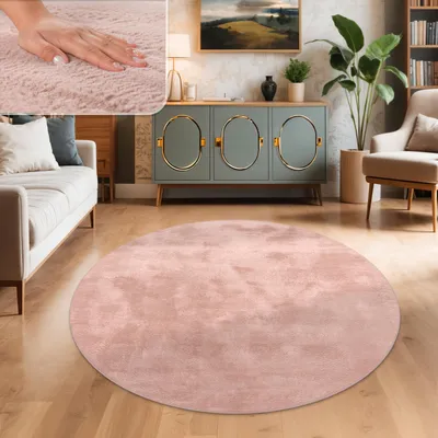 A circular pink rug is placed on a wooden floor in a living room setting, with a sofa, a cabinet, and a chair visible.