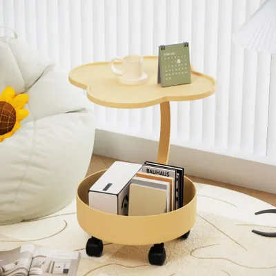 A small yellow side table with two tiers, placed on a rug next to a white beanbag chair. The top tier holds a mug and a calendar, while the bottom tier contains books and a box. The table has wheels.