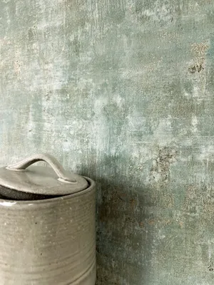 A close-up of a ceramic container with a lid against a textured, distressed green and gray wall.