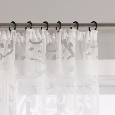 A close-up view of white sheer curtains with a floral pattern hanging from a curtain rod.