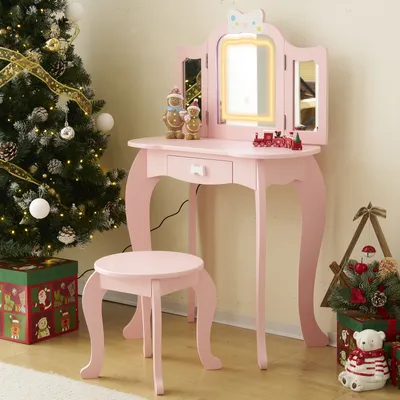 A pink children's vanity set with a stool is set up next to a decorated Christmas tree, with Christmas-themed gift boxes and a small decorative tree nearby.