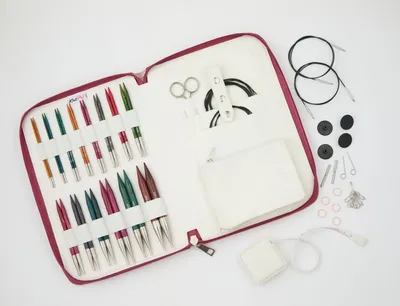 An open knitting needle set case with various knitting needles and accessories laid out on a white background.