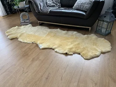 A sheepskin rug is laid out on a wooden floor in front of a black leather sofa. A decorative lantern is placed next to the sofa.