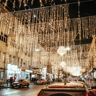 A street decorated with numerous strings of warm white fairy lights at night.