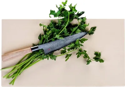 A knife is placed on a bunch of parsley on a cutting board.
