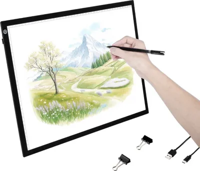 A hand is using a stylus to draw on a light pad displaying a landscape.