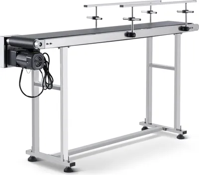 A long, silver conveyor belt system with a black belt, supported by a metal frame, is shown against a white background. A black motor is attached to the left end of the conveyor belt.