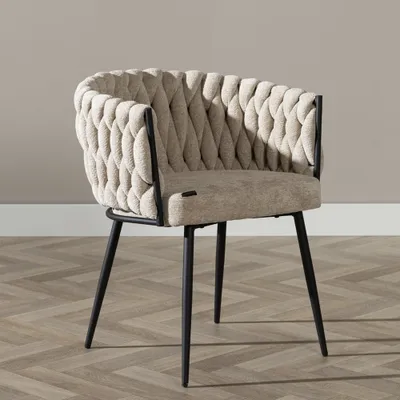A beige upholstered chair with black metal legs is shown against a light gray wall and a wooden floor.