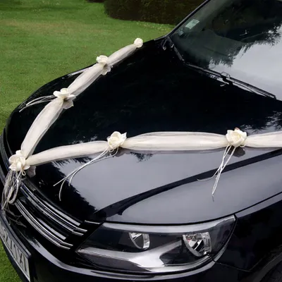 Cremefarbene Organza-Girlande mit Rosenblüten in V-Form auf der Motorhaube eines schwarzen Autos als elegante Hochzeitsdekoration befestigt.