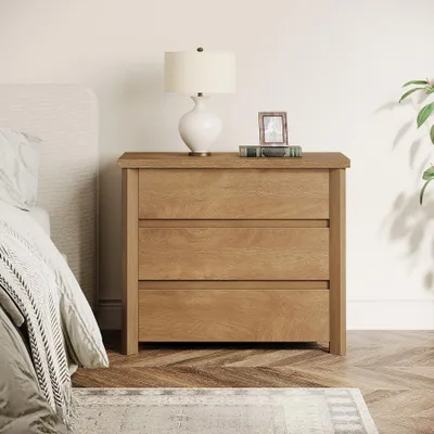 A bedside table with a lamp and a framed picture on top, next to a bed.