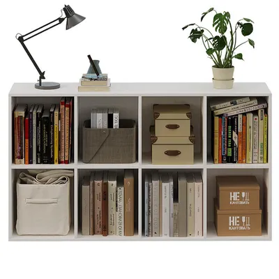 A white shelving unit filled with books, decorative boxes, a plant, and a lamp.