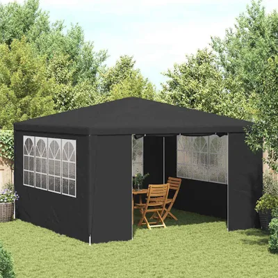 A black party tent set up in a grassy backyard with trees in the background. A wooden table and chairs are inside the tent.