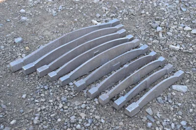 Several curved metal pieces laid out on a gravel surface.