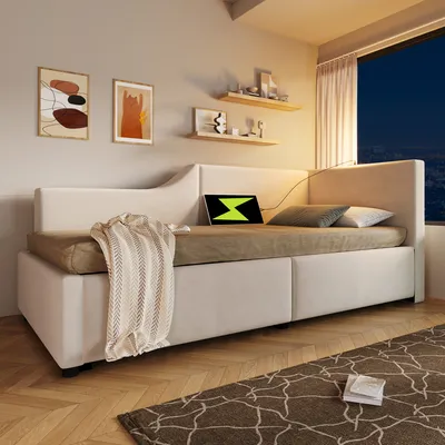 A modern bedroom or living room setting with a beige sofa bed, decorative pillows, a blanket, and artwork on the wall.
