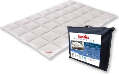 A white down comforter is laid out diagonally, with a dark blue carrying bag for the comforter placed to its right.