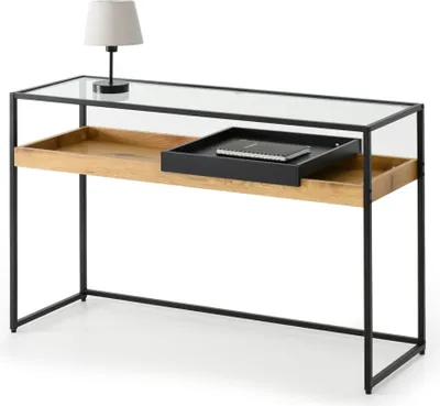 A console table with a glass top, wooden shelf, and black metal frame, featuring a lamp and a tray with a notebook.