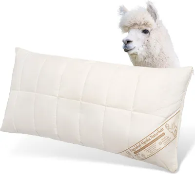 A cream-colored pillow with a quilted pattern is shown diagonally, with the head of a white alpaca peeking over the top right corner.