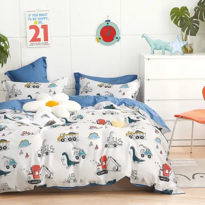 A child's bedding set with a dinosaur and construction vehicle theme is displayed on a bed.