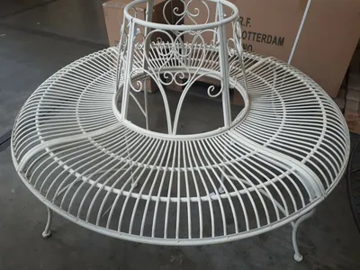 A white metal garden bench with a circular seat and a conical backrest, placed indoors on a concrete floor with cardboard boxes in the background.