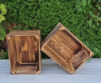 Two wooden crates are placed on a gray surface in front of a green hedge.