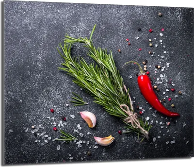 A close-up overhead shot of fresh rosemary sprigs, a red chili pepper, garlic cloves, coarse salt, and peppercorns scattered on a dark, textured surface.