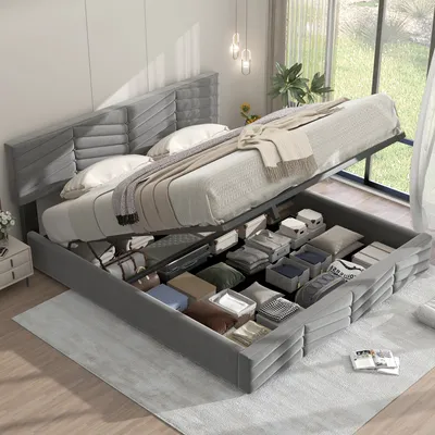 A grey upholstered bed with its storage compartment open, revealing neatly organized items inside. The bed is in a well-lit room with a large window in the background.