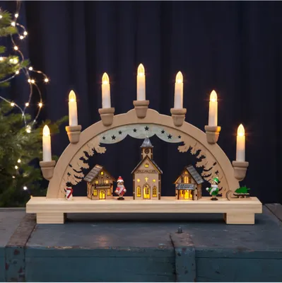 A wooden Christmas arch with illuminated houses and candle-like lights.