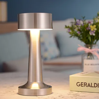 A silver table lamp is placed on a marble surface, with a vase of flowers and a book in the background.