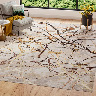 A rug with a marble-like pattern is laid out on a wooden floor in a living room setting. A gray armchair with cushions and a yellow throw is placed on the left side of the rug. A window with a view of green trees is visible in the background.