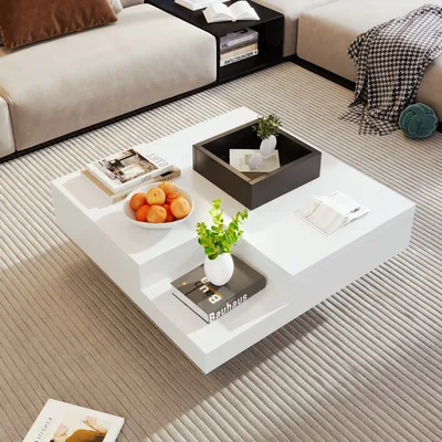 A white, multi-level coffee table sits on a striped rug in a modern living room. It holds decorative items including books, fruit, and plants.