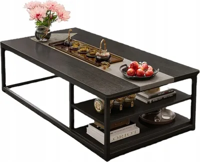 A dark wood coffee table with shelves, decorated with a vase of pink flowers, a tea set, and a bowl of red apples.
