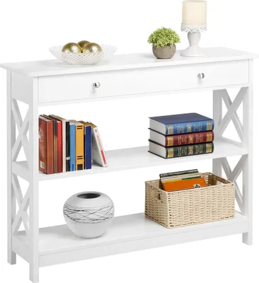A white console table with shelves and a drawer, decorated with books, a plant, a candle, and decorative spheres.