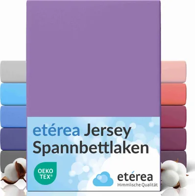 A stack of folded jersey fitted sheets in various colors, with the main product in violet prominently displayed. Cotton bolls are visible in the foreground.