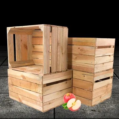 Several wooden crates are stacked, with two apples and leaves in the foreground.