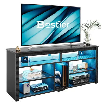A modern TV stand with a large television on top and various electronic devices and decorative items on its shelves, illuminated by blue LED lights.