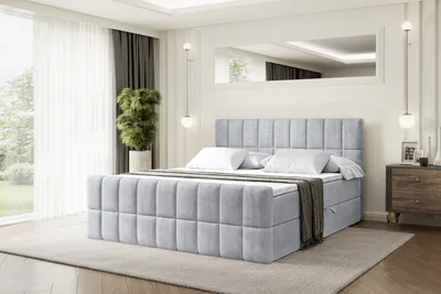 A bedroom scene with a bed as the main focus, set against a large window with sheer curtains and a dresser to the side.