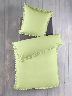 A top-down view of a green duvet cover and pillowcase set with ruffled edges, laid out on a wooden floor.