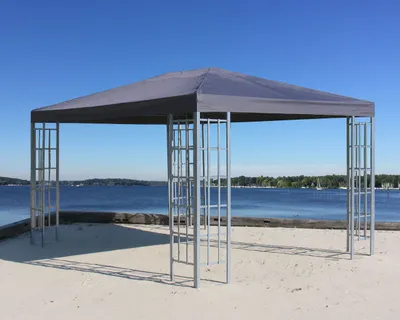 A gray gazebo stands on a sandy beach with a blue lake and sky in the background.
