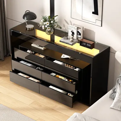 A modern black sideboard with multiple open drawers, displaying various items inside, set in a well-lit room with a wooden floor and a large piece of art on the wall.