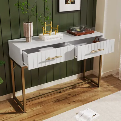 A white console table with gold legs and two open drawers, placed against a dark green paneled wall.