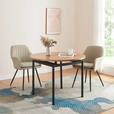 A round dining table with two chairs in a room with a rug and artwork.