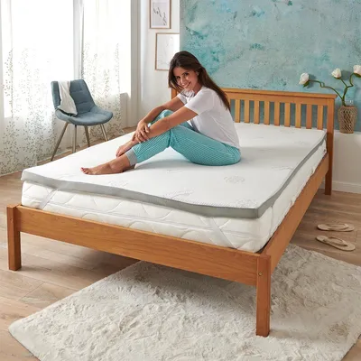 A woman sitting on a mattress topper on a bed in a bedroom.